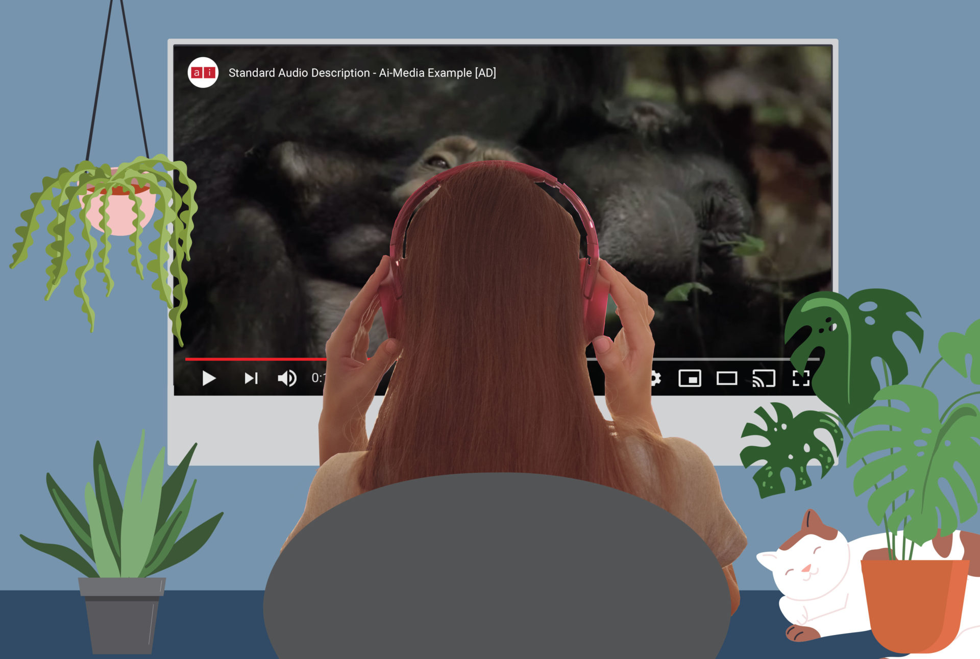 A person sitting at a desk with headphones on, using audio description to listen to a video playing on the computer in front of them. There are plants on the desk and a cat asleep on the right-hand side.